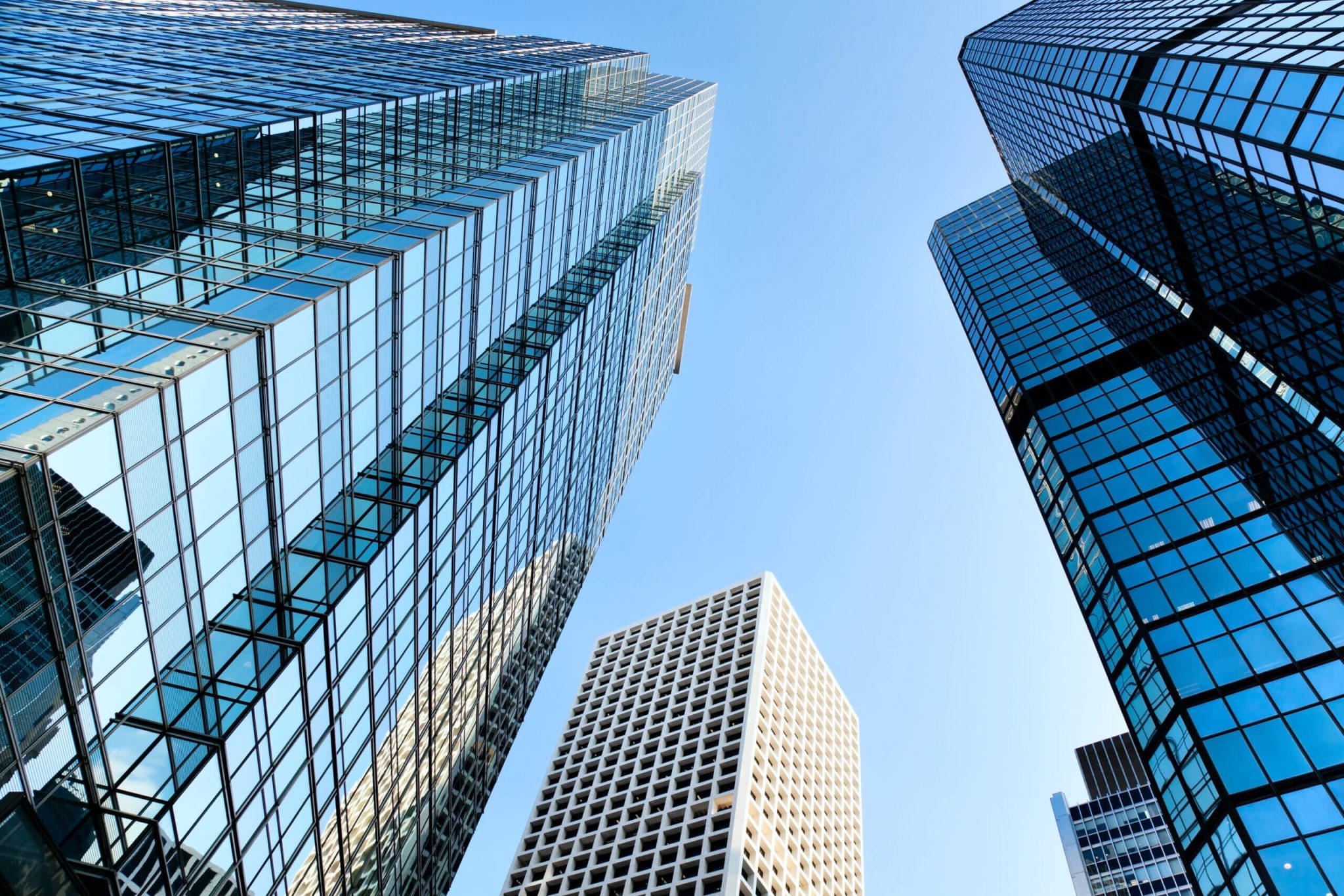 Four tall glass office buildings in a downtown setting, seen from the ground up, toward a blue sky. This represents our expertise in networking software systems. Enterprise software integration is our niche.